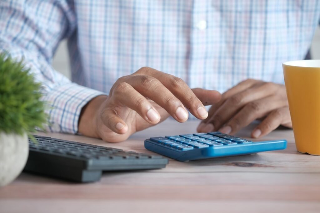 Bookkeeper working with a blue calculator, keyboard, and plant on a bright desk
