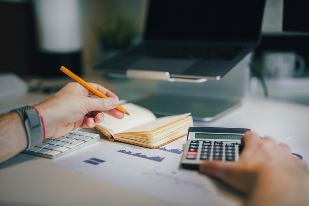 Hands taking notes beside printed charts and a calculator