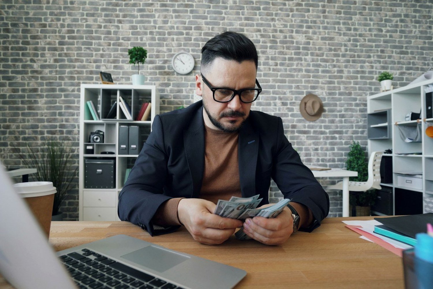 Business owner counting cash at an office desk beside a laptop